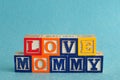 The words love mommy spelled with alphabet blocks against a blue