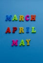 Words `March, April, May` from colored plastic magnets on blue paper background