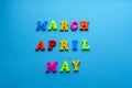 Words `March, April, May` from colored plastic magnets on blue paper background