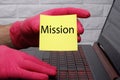 The words mission on yellow paper in a man`s red-gloved hand.