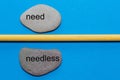 The words need and needless are written on natural smooth stones separated by a yellow pencil. The background is isolated in blue