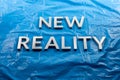 The words new reality laid with white letters over crumpled blue plastic film background - slanted perspective