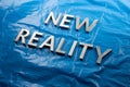 The words new reality laid with white letters over crumpled blue plastic film background - slanted perspective