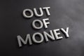 The words out of money laid with white brushed metal letters on flat black surface with diagonal composition and selective focus