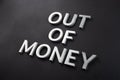 The words out of money laid with white brushed metal letters on flat black surface with diagonal composition and