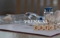 Words PRENATAL CARE composed of wooden dices. Pills, documents and a pen in the background