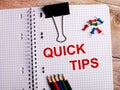 The words QUICK TIPS is written in a notebook near multi-colored pencils and buttons on a wooden background Royalty Free Stock Photo