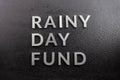 The words rainy day fund laid with silver metal letters on black background, covered with water drops, flat lay perspective,