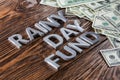 Words RAINY DAY FUND laid on wooden surface by metal letters with rain drops and us dollar banknotes