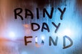 Words RAINY DAY FUND written by hand on wet glass at night with blurry street light background