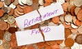 The words retirement fund written in purple pen on white paper on top of a pile of British coins