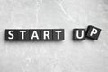 Words START UP made with black cubes on grey marble background, flat lay