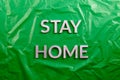The words stay home laid with silver metal letters on crumpled green plastic background in flat lay perspective