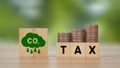 Words TAX and coin money stack on a wooden cube with co2 icon. Carbon tax, CO2 tax, environmental and social responsibility