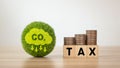 Words TAX and coin money stack on a wooden cube with Co2 icon on a green ball. Carbon tax, CO2 tax, environmental and social