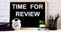 The words TIME FOR REVIEW is written on the chalkboard next to the white alarm clock, glasses, potted plant, and pencils in a Royalty Free Stock Photo