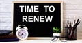 The words TIME TO RENEW is written on the chalkboard next to the white alarm clock, glasses, potted plant, and pencils in a stand Royalty Free Stock Photo