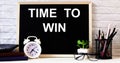 The words TIME TO WIN is written on the chalkboard next to the white alarm clock, glasses, potted plant, and pencils in a stand Royalty Free Stock Photo