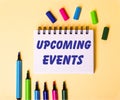 The words UPCOOMING EVENTS written in a white notebook on a beige background near multi-colored markers Royalty Free Stock Photo