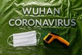 Words wuhan coronavirus laid with metal letters on green crumpled plastic film backdrop with face masks and thermometer