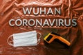 Words wuhan coronavirus laid with metal letters on orange crumpled plastic film backdrop with face masks and thermometer