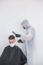 The work of the barber during the coronavirus, the hairdresser trim the client in a mask and a protective suit, quarantine