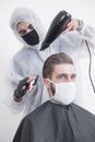 The work of the barber during the coronavirus, the hairdresser trim the client in a mask and a protective suit, quarantine