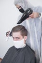 The work of the barber during the coronavirus, the hairdresser trim the client in a mask and a protective suit, quarantine