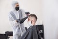 The work of the barber during the coronavirus, the hairdresser trim the client in a mask and a protective suit, quarantine