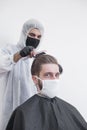 The work of the barber during the coronavirus, the hairdresser trim the client in a mask and a protective suit, quarantine