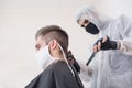 The work of the barber during the coronavirus, the hairdresser trim the client in a mask and a protective suit, quarantine