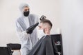 The work of the barber during the coronavirus, the hairdresser trim the client in a mask and a protective suit, quarantine