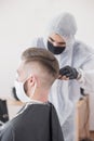 The work of the barber during the coronavirus, the hairdresser trim the client in a mask and a protective suit, quarantine