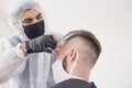 The work of the barber during the coronavirus, the hairdresser trim the client in a mask and a protective suit, quarantine