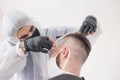 The work of the barber during the coronavirus, the hairdresser trim the client in a mask and a protective suit, quarantine