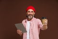 Work and coffee concept. Smiling mature man in casual clothing holds tablet in hand while offering craft cup with coffee Royalty Free Stock Photo