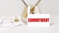 Work desk with gold glasses, pen, white card with the text COMMITMENT Business concept. Home Office. Workplace close-up Royalty Free Stock Photo
