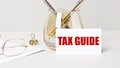 Work desk with gold glasses, pen, white card with the text TAX GUIDE. Business concept. Home Office. Workplace close-up Royalty Free Stock Photo