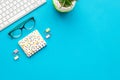 Work desk of manager. Computer keyboard, glasses, stationery, plant on blue background top view copy space