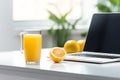 work desk near the window with a laptop and a glass of orange juice, plant and other items. Morning light. Work at home
