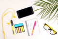 Work desk with open notebook, glasses, phone, headphones and palm leaf, top view. Summer mockup, flat lay. Minimal style