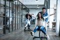 Work hard play hard. Four young cheerful business people in smart casual wear having fun while racing on office chairs and smiling Royalty Free Stock Photo