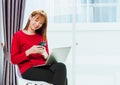 Woman smiling using mobile phone while typing message text during working with laptop computer at home office Royalty Free Stock Photo