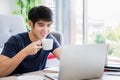 Work from home concept. Happy handsome man sitting drinking coffee and working at home by computer laptop Royalty Free Stock Photo