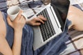 Work from home during quarantine. Young woman in a blue towel is typing on her laptop with a white cup in her hands. Relaxing by Royalty Free Stock Photo