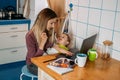 Work from home. Young mother with baby girl working at home using laptop on kitchen background Young woman feeding her baby, Royalty Free Stock Photo