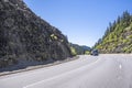 Work horse blue big rig semi truck transporting cargo on flat bed semi trailer driving on the mountain winding road with rock Royalty Free Stock Photo