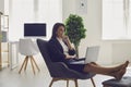 Work online at home. A young business woman sits comfortably working with a laptop in an armchair in an office room at Royalty Free Stock Photo