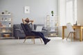 Work online at home. Young man with hands behind his head dreams of sitting in a chair with a laptop in a living room at Royalty Free Stock Photo