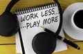 WORK LESS ... PLAY MORE - words on a white notepad on a yellow background with headphones, a cup of coffee and a pen